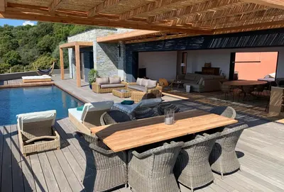 a patio with a wooden table and chairs next to a pool at Schena Villata in Zonza
