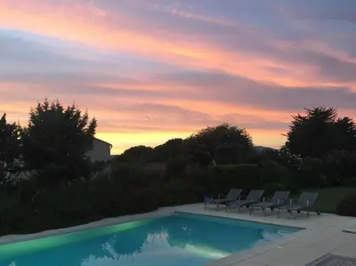 a pool with chairs and a sunset in the background at Appartement bord de mer avec piscine privee Porticcio in Porticcio