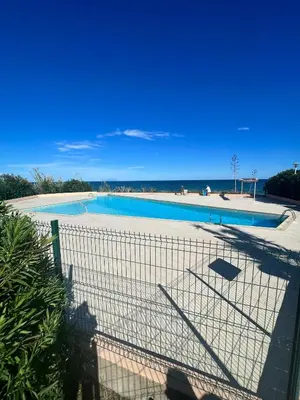 a fence around a swimming pool next to the beach at Studio pied dans l'eau - WIFI- Piscine in Santa-Lucia-di-Moriani