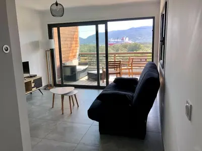 a living room with a black couch and a balcony at Studio Piscine, 200m port de Porto Vecchio pour 2 personnes in Porto-Vecchio
