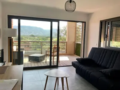 a living room with a black couch and a balcony at Studio Piscine, 200m port de Porto Vecchio pour 2 personnes in Porto-Vecchio