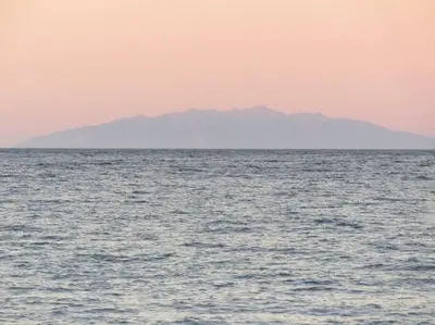 a large body of water with a mountain in the background at Appt dans résidence avec piscines et plage privées in San-Nicolao