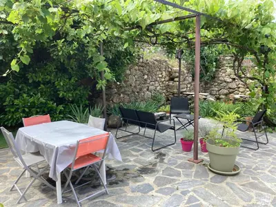 a patio with a table and chairs and an umbrella at Maison Kyprea: charmant appartement /duplex , spacieux, tout confort avec terrasse extérieure privée, parking privatif , vue pittoresque sur la citadelle de Corté et les montagnes. in Corte