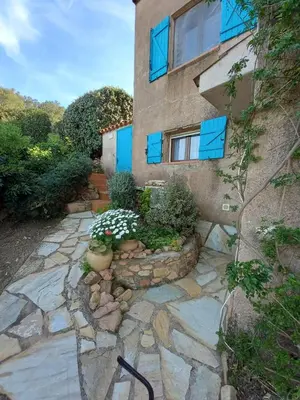 a house with blue windows and a stone walkway at appartement climatisé 35 m2 pour 1 couple - piscine partagée - in Porto-Vecchio