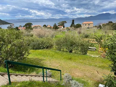a green rail in a field with a house and water at Lavallee in Campomoro