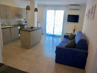 a living room with a blue couch and a kitchen at Les bougainvilliers in Penta-di-Casinca