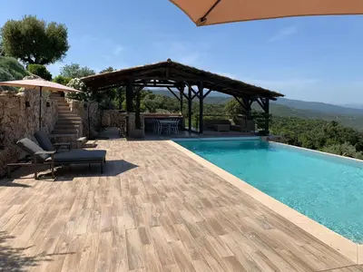 a swimming pool with a wooden deck and a pergola at U CASEDDU- Villa piscine privée chauffée- vue mer- clim-wifi in Sari Solenzara