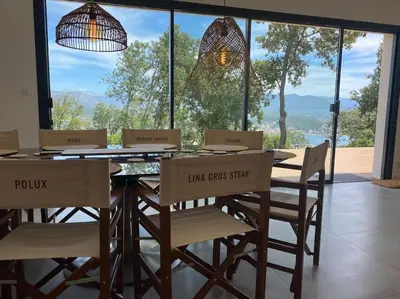 a dining room with a table with chairs and a large window at Villa d'Architecte Casa Mado avec Piscine vue imprenable in Ajaccio
