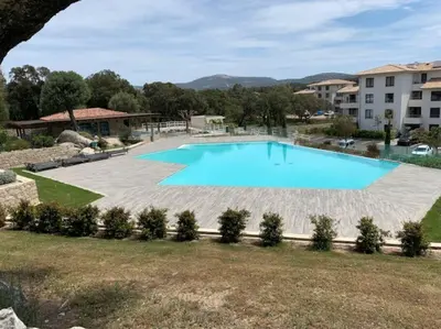 a large swimming pool in a yard next to a building at T2 neuf 4 personnes avec piscine/terrain tennis in Porto-Vecchio