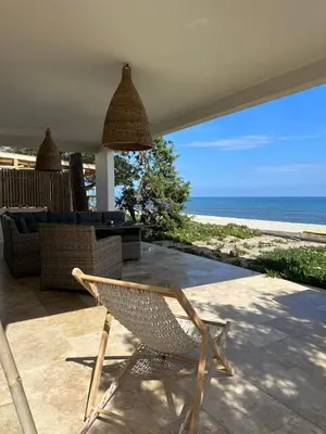 a wicker chair sitting on a patio overlooking the ocean at Maison les pieds dans l’eau in Ghisonaccia