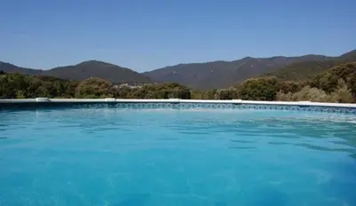 a large blue swimming pool with mountains in the background at Gites Chalets de Grosseto-Prugna in Grosseto-Prugna