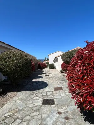 a stone walkway next to a building with red bushes at VILLA T3 bord de mer - vue mer à 500 m de la plage- piscine chauffée A CASETTA DI A SPIAGGIA in Cervione