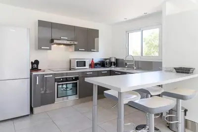 a white kitchen with a white table and chairs at Villa 4 personnes U Pinu, piscine partagée, 6 kms de porto vecchio in Porto-Vecchio